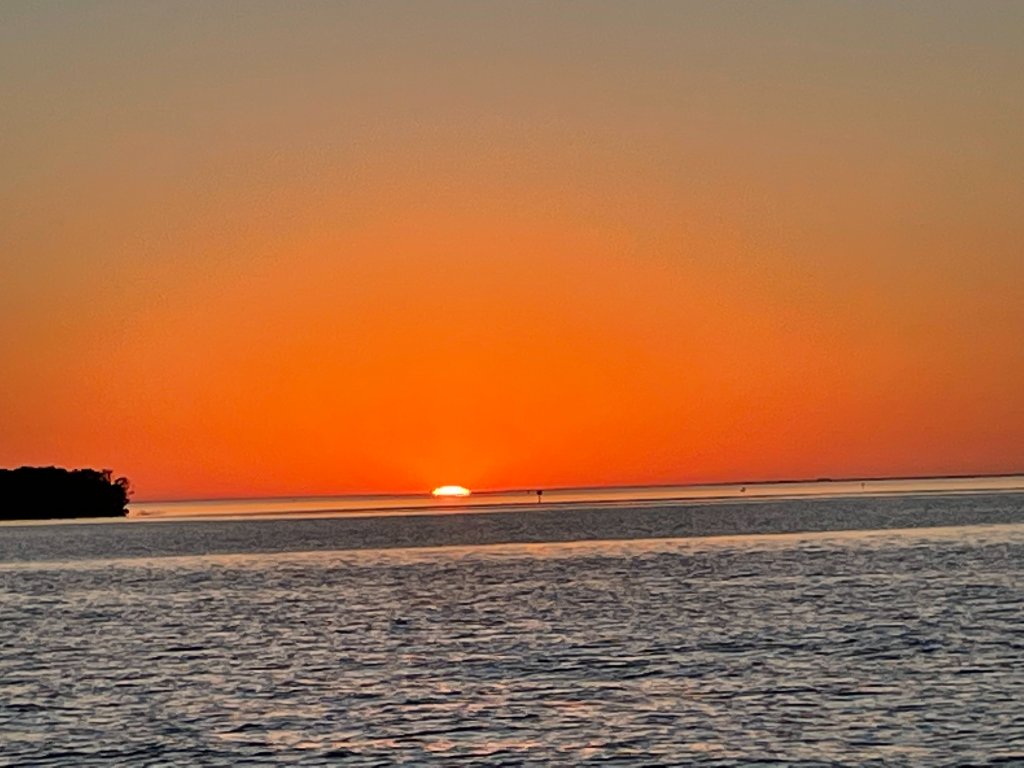 Golden sun sitting at the horizon over calm water at sunset