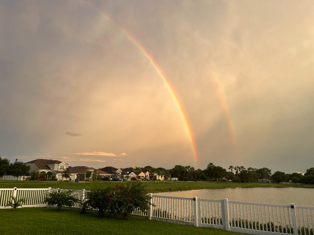 Double rainbow arching over the lakefront with white picket fence