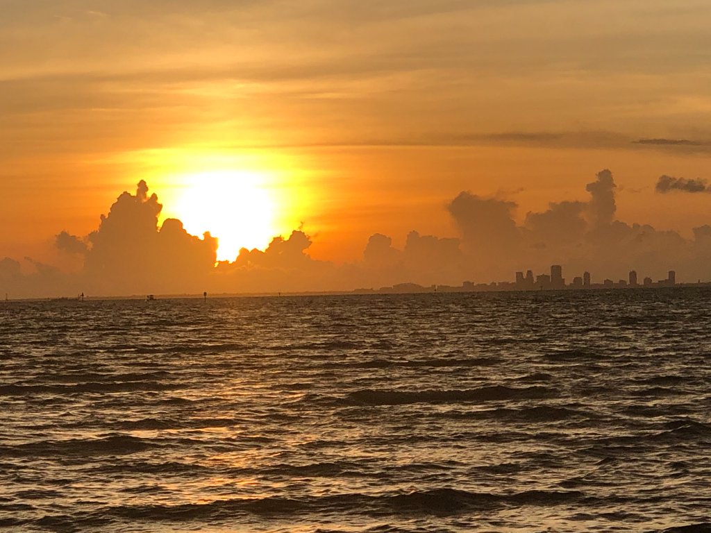 Sunset over water with sun peeking through dark cumulus clouds and distant skyline
