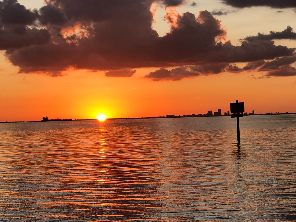 Vibrant orange sunset over water with ship silhouette and navigation marker