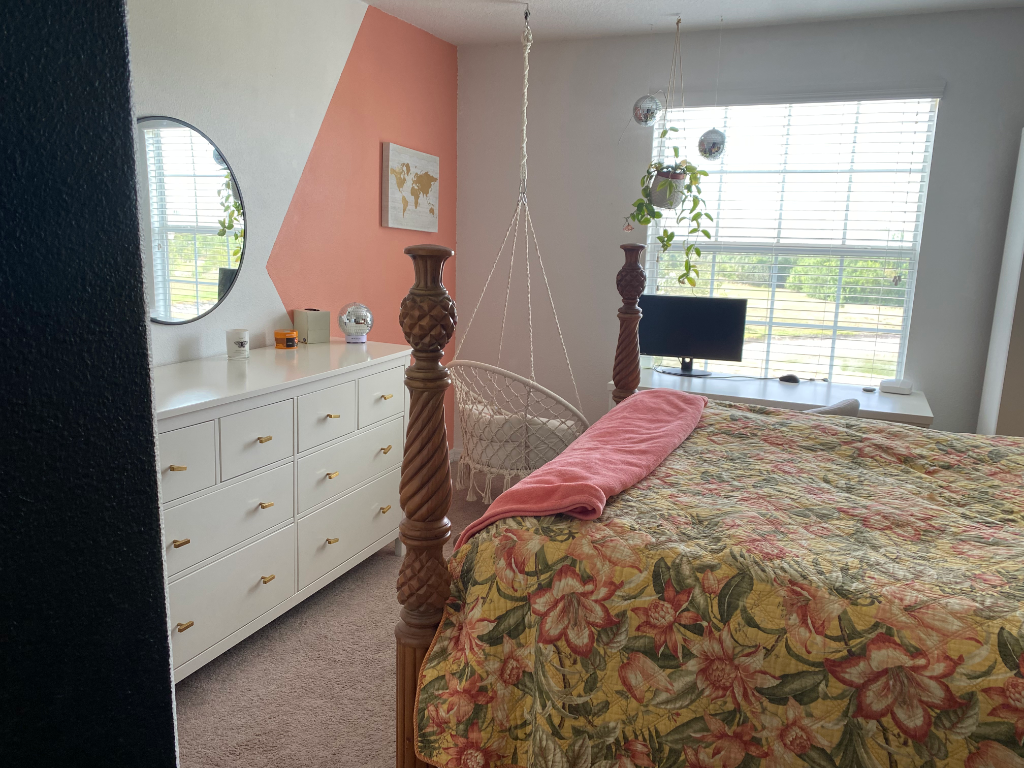 Bedroom with macrame swing chair, peach accent wall, and four-poster bed