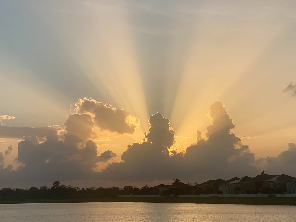 Golden sunset with crepuscular rays beaming behind cumulus clouds over the Mira Lago pond