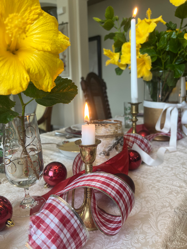 Holiday dining table with yellow hibiscus, red ornaments, and candlelight