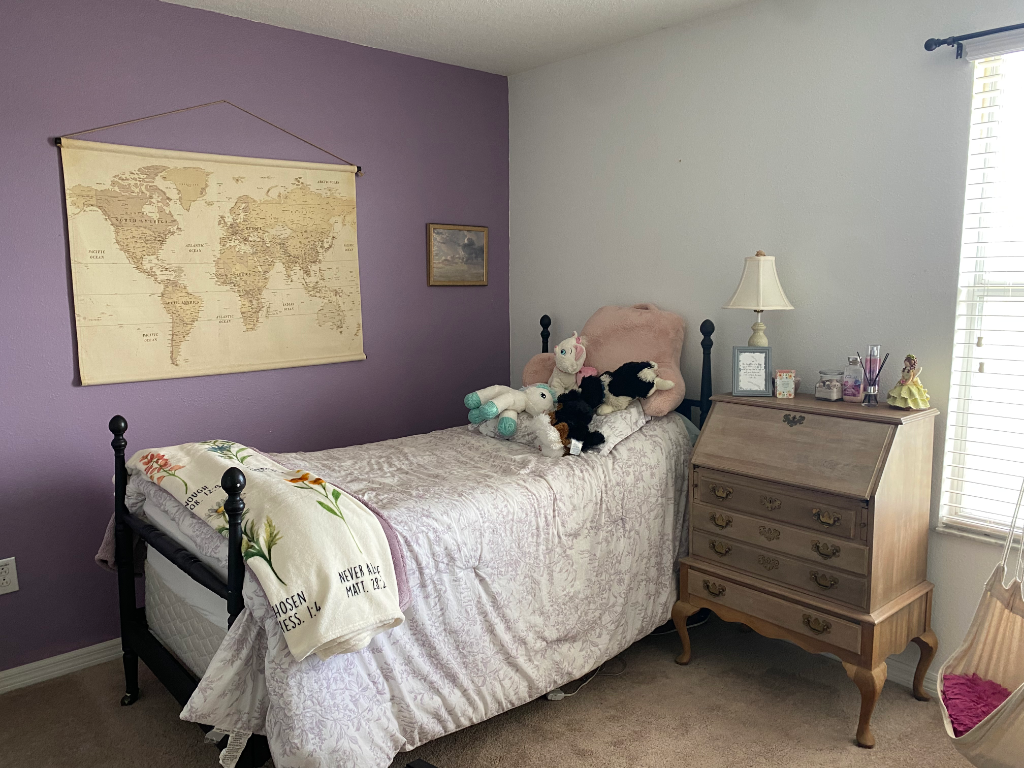 Bedroom with patterned comforter, desk, nightstand, and world map on purple wall