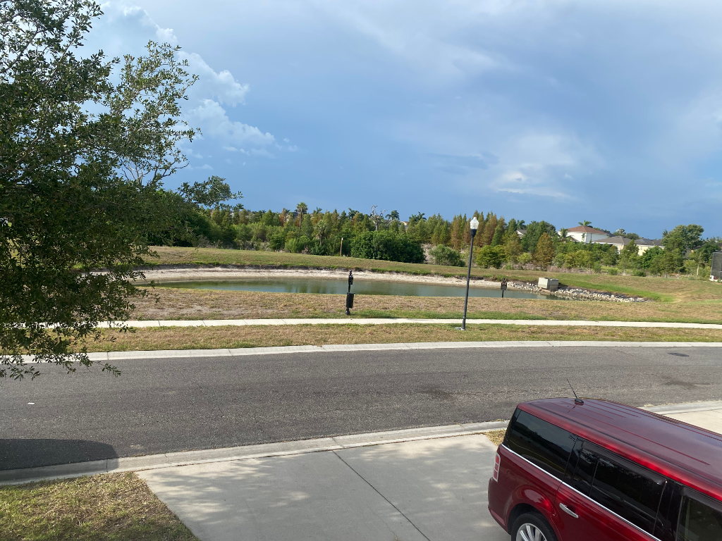 View of the front yard and street from an elevated angle, with a retention pond and dramatic storm clouds rolling in