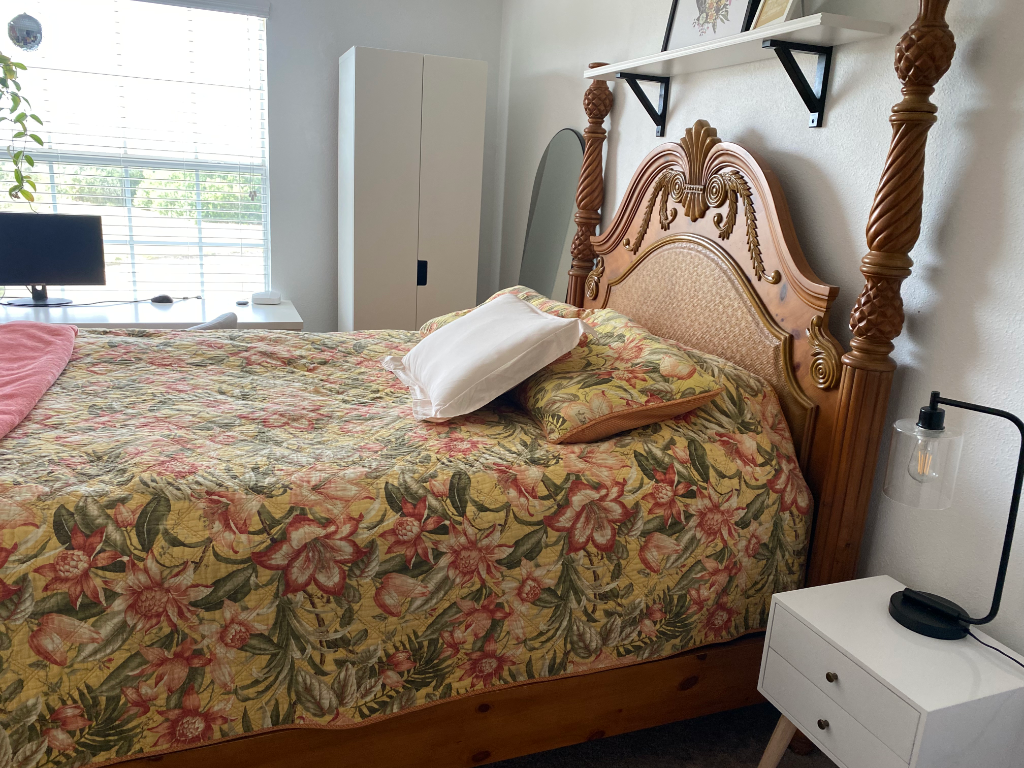 Bedroom with wooden four-poster bed, floral quilt, and nightstand with lamp