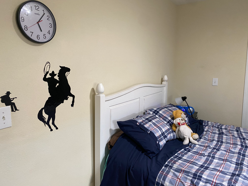 Bedroom with cowboy and guitar wall decals, navy plaid bedding, and clock