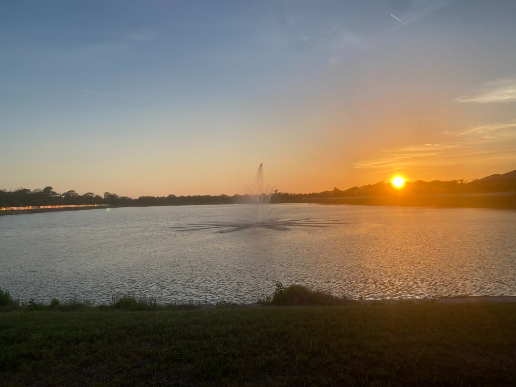 Golden sunset over the Mira Lago pond with fountain silhouetted against an orange sky