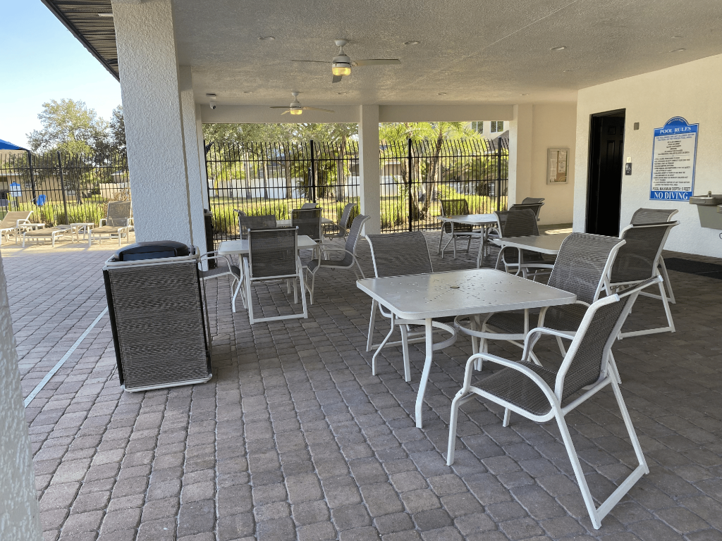 Covered poolside seating pavilion with tables, chairs, and pool rules sign