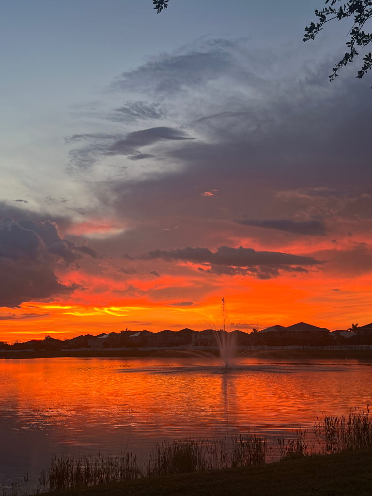 Brilliant orange and red sunset reflected on the pond with fountain spray