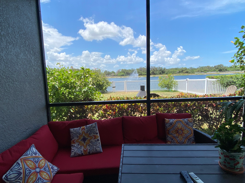 Screened lanai with red sectional sofa, decorative pillows, and pond fountain view
