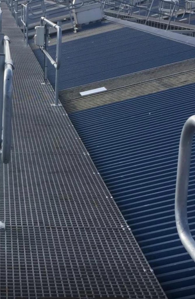 Commercial industrial roof showing metal grating walkway alongside coated corrugated roof surface with safety handrail system and roof plant.