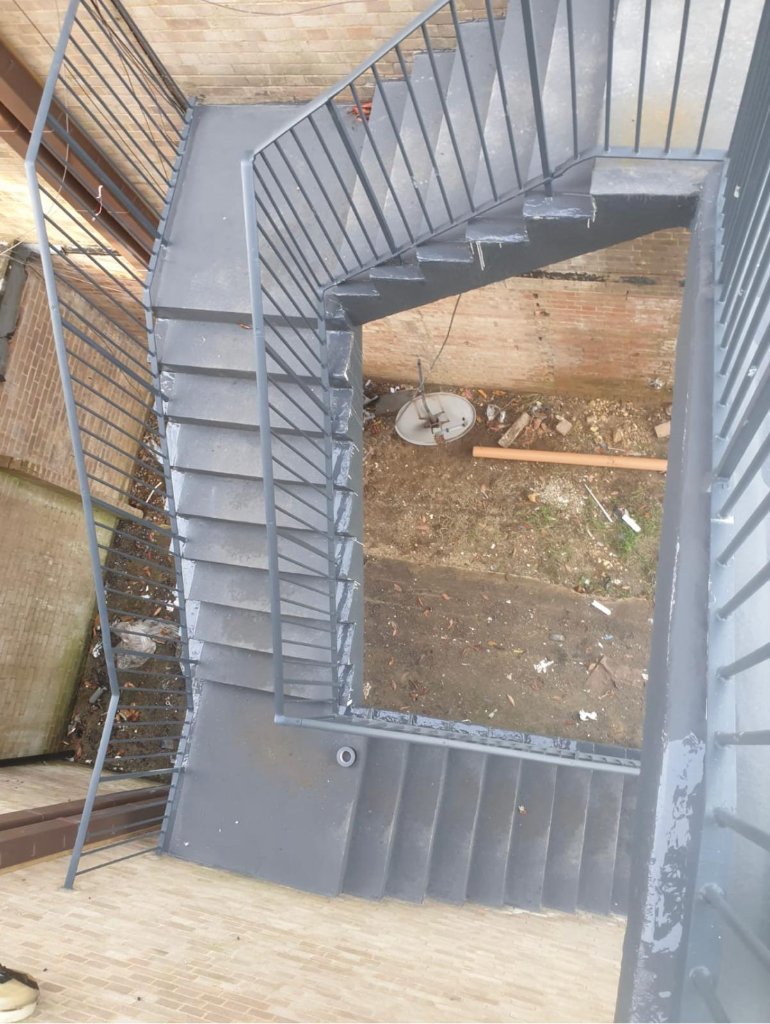 Spray-applied coating on external staircase — treads, risers and stringers fully coated in grey