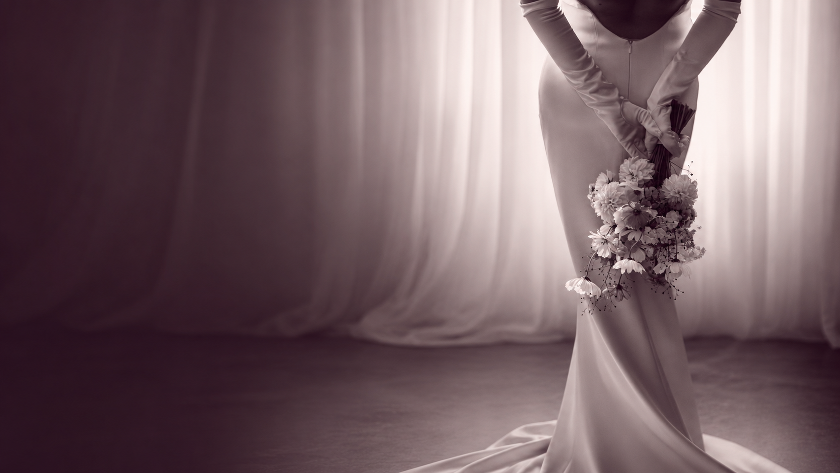 A bride in a backless white gown holding a soft bridal bouquet, framed by draped fabric — Hannah's Ever Afters private planning experience