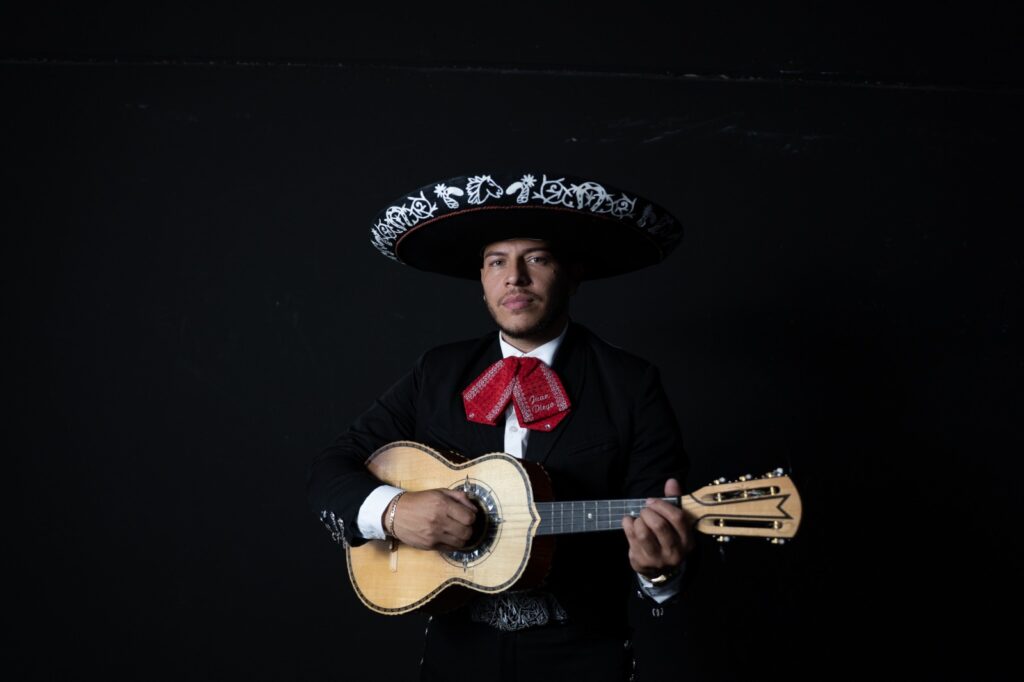 Músico mariachi con vihuela posando con sombrero charro en fondo oscuro