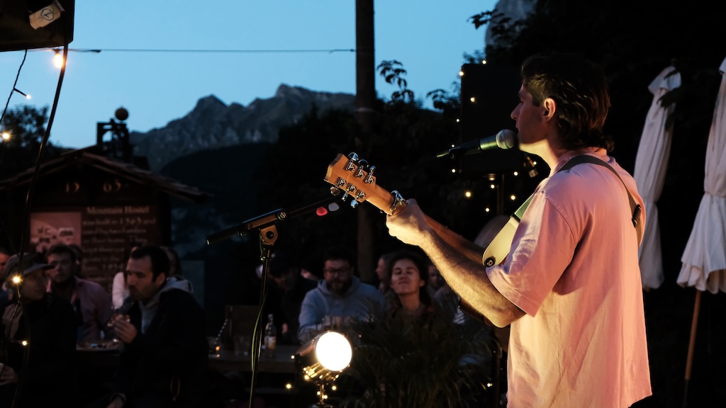 Acoustic guitarist performing at twilight with mountain backdrop