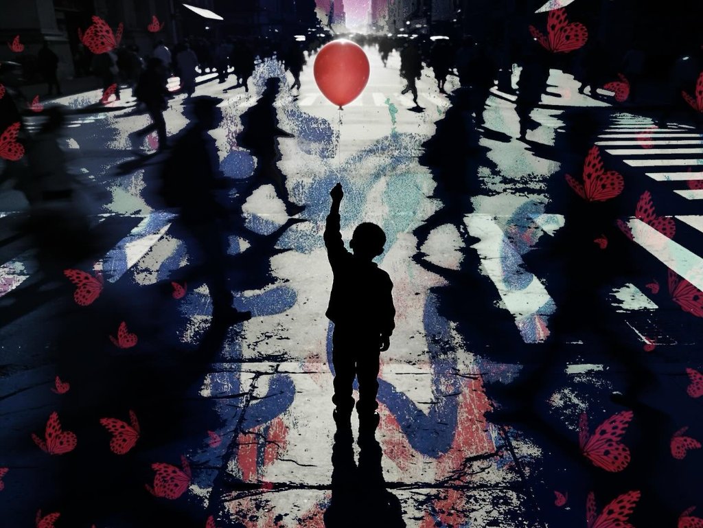 Boy silhouette raising a red balloon amid a crowd on a city street