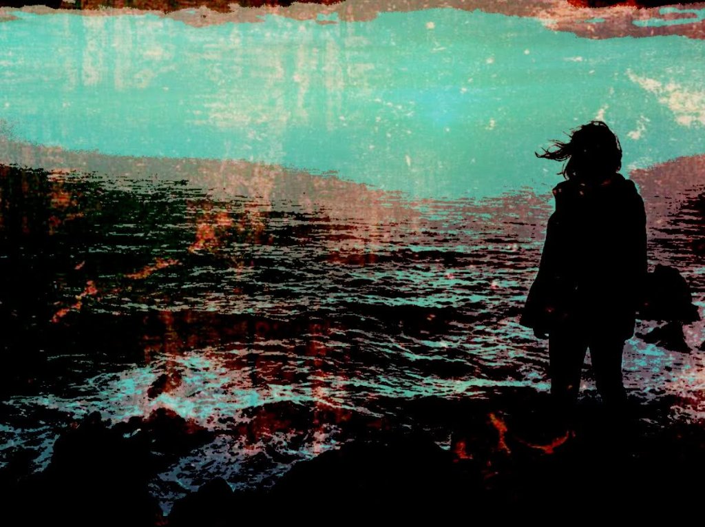 Woman silhouette standing on rocks watching a teal ocean horizon