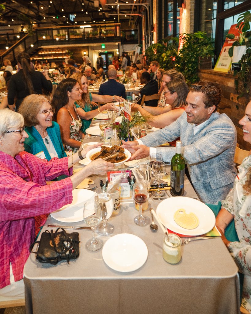 Art vs. Food — guests laughing and passing plates of food across a long dinner table