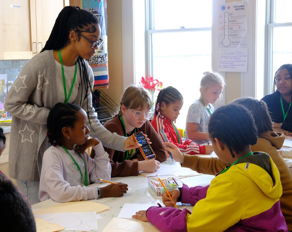 Teen mentor guiding students through a drawing activity at A.I.R. Academy