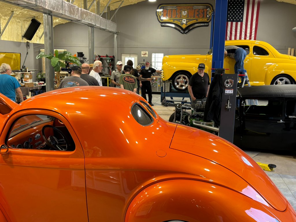 Inside the shop — guests admiring the orange Willys coupe and yellow custom