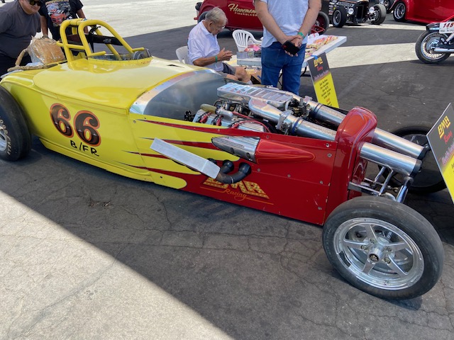 Silver open-wheel roadster with exposed engine — show field