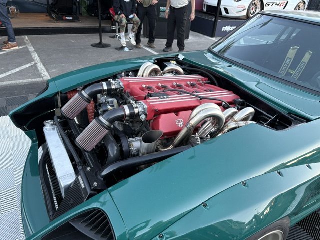Teal Datsun Z engine bay — twin-turbo red V8, outdoor SEMA grid