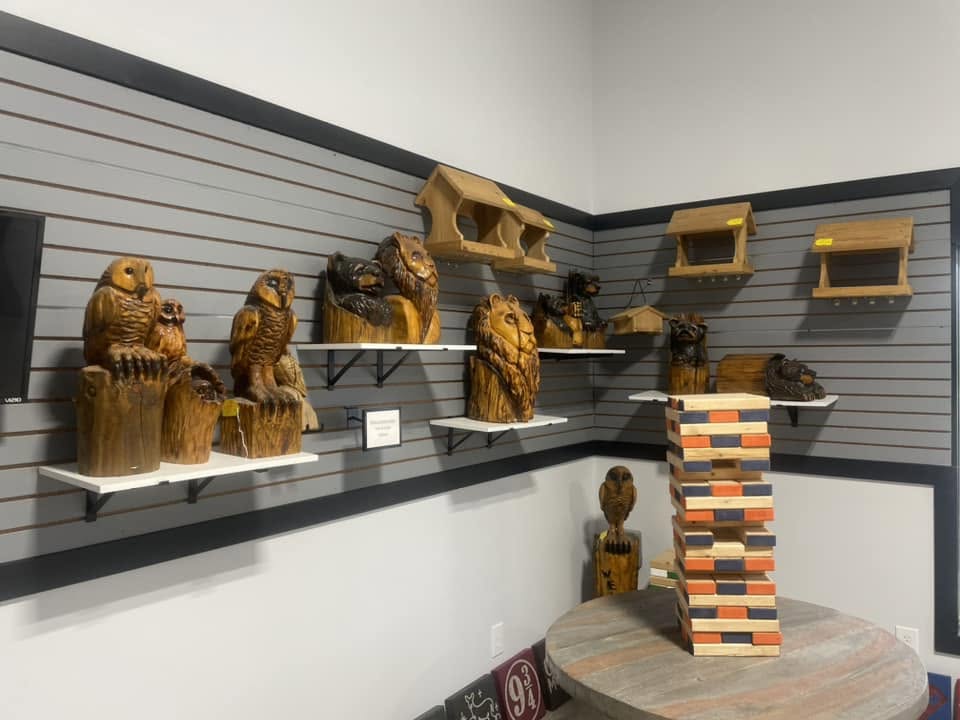 Round table with a Jenga-style block tower of orange black and natural wood blocks, with carved wooden owl bear and lion sculptures on wall shelves