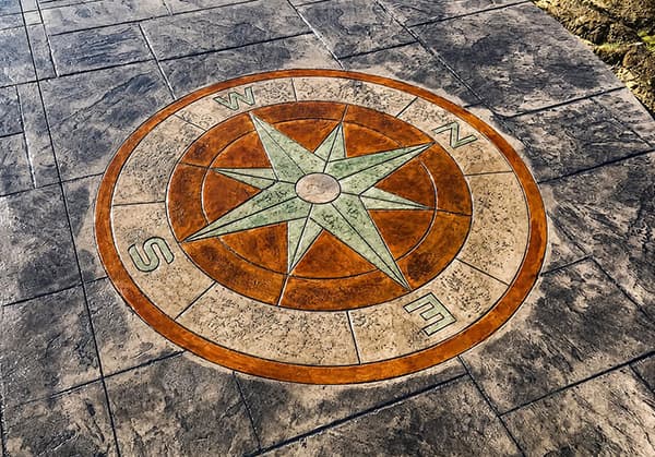 Circular compass rose stained concrete inlay with sage green star points and terracotta ring set in a charcoal stamped patio