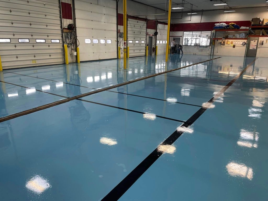 High-gloss light blue epoxy floor in an industrial garage with yellow support columns and reflective surface