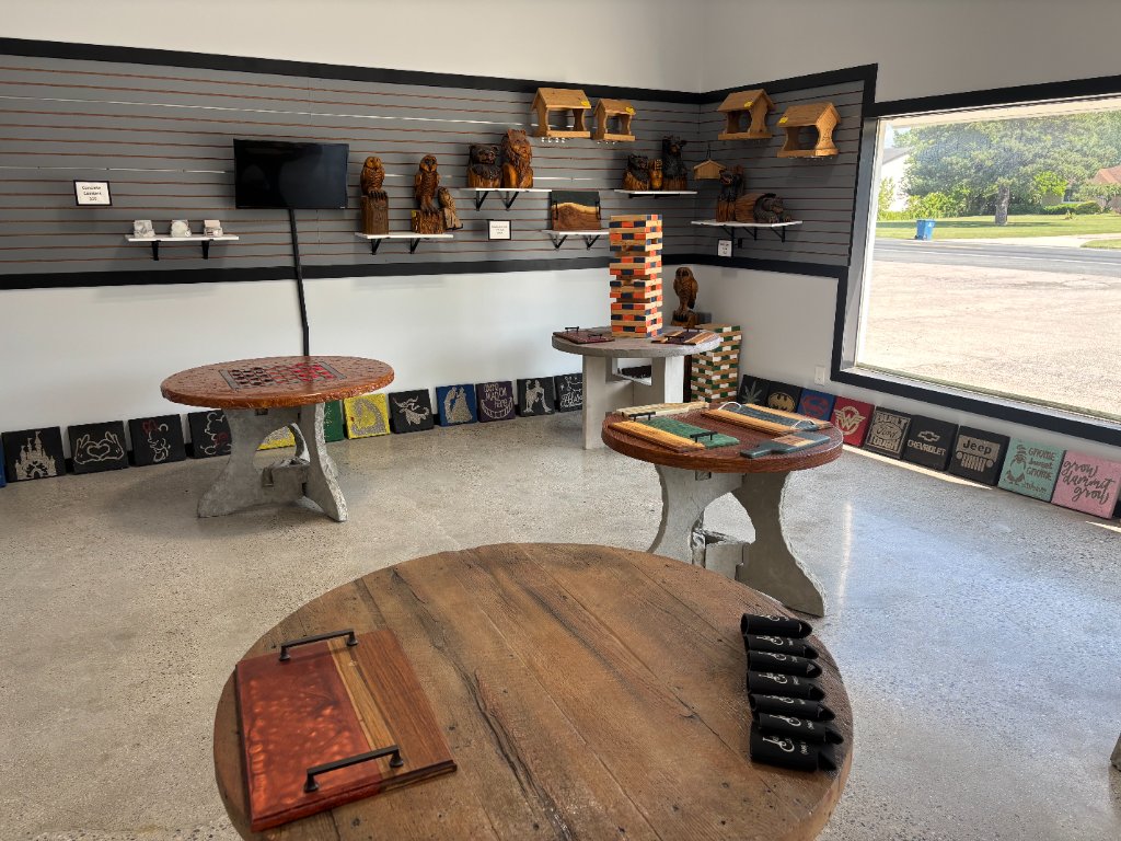 Showroom interior with round wood-top concrete tables, floating shelves of handcrafted items, and patriotic and brand logo tiles along the floor