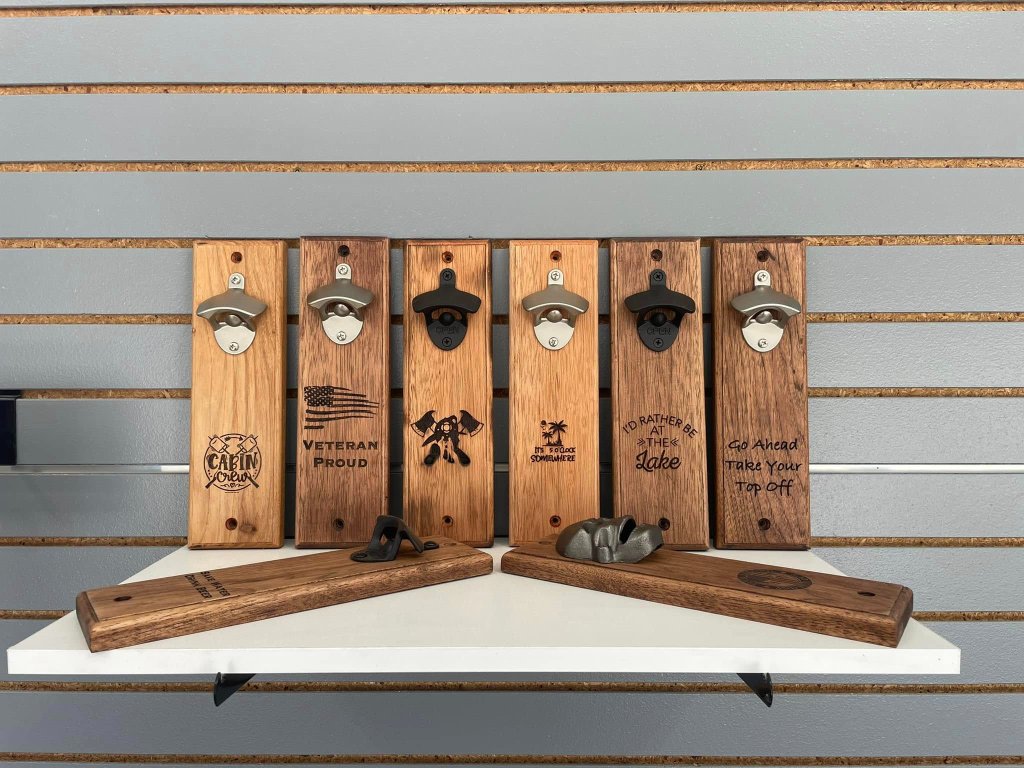 Wall-mounted wooden bottle openers with engraved sayings including Veteran Proud, Cabin Crew, It's 5 O'Clock Somewhere, and I'd Rather Be At The Lake