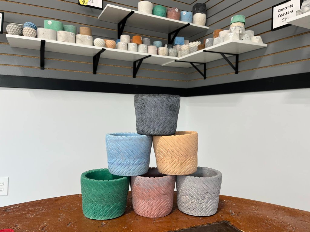 Six chevron-patterned concrete planters stacked in a pyramid on a round wooden table in colors including charcoal, sky blue, peach, emerald, dusty rose, and grey