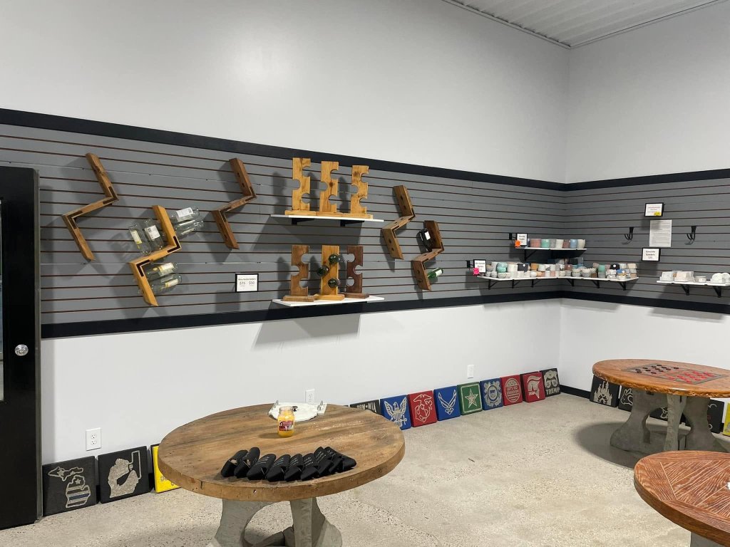 Showroom wall display with geometric wooden wine bottle racks, floating shelves holding small colored concrete pots, and decorative logo plaques along the floor