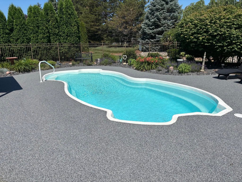 Vuba Stone resin-bound surfacing surrounding a kidney-shaped swimming pool, showing fine speckled grey aggregate deck with turquoise pool water