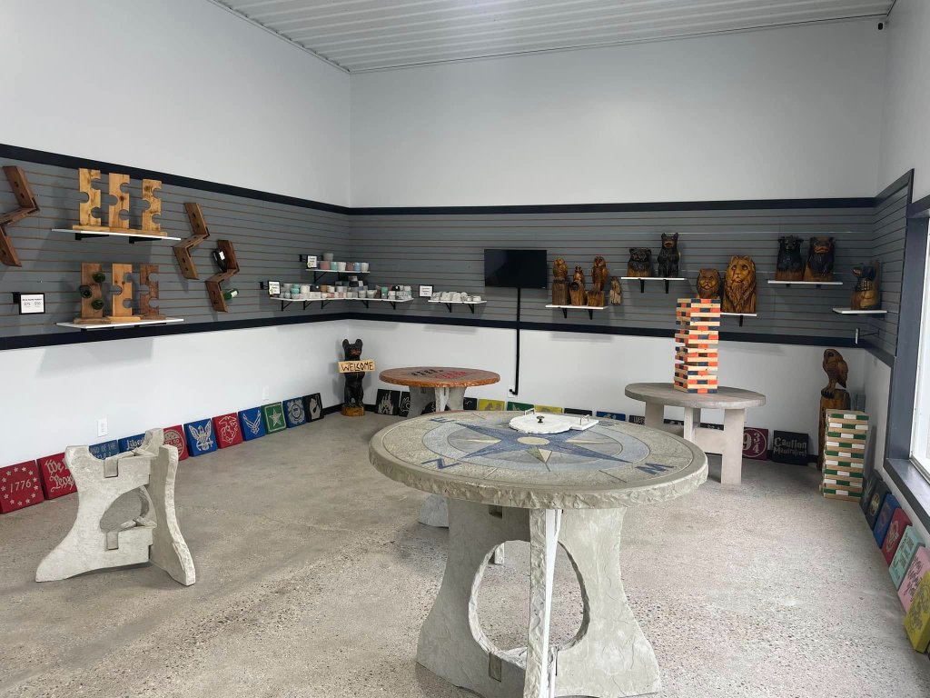 Showroom display wall featuring wood-carved animals, wine bottle racks, painted signs, and concrete coasters on slat-wall shelving