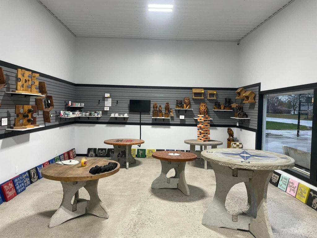 Showroom interior with round concrete tables, a compass rose inlay table, wood carvings, and decorative plaques displayed on grey slat-wall