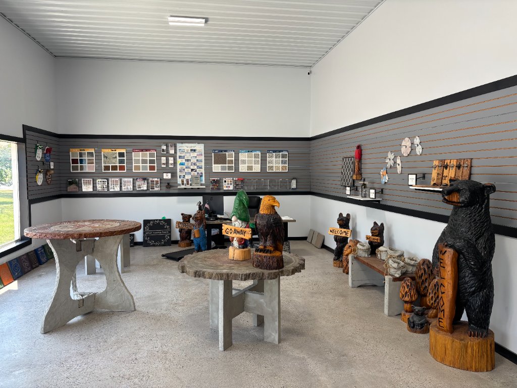 Showroom floor with a round wood table holding a carved eagle and a GO AWAY gnome, a carved welcome bear, and a compass rose table in the background