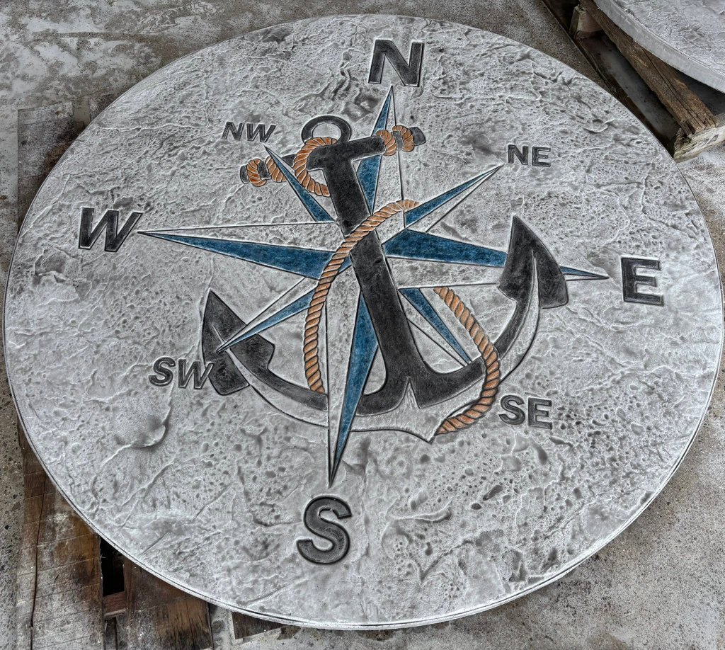 Circular stamped concrete piece with a nautical compass rose and anchor inlay on a wooden pallet
