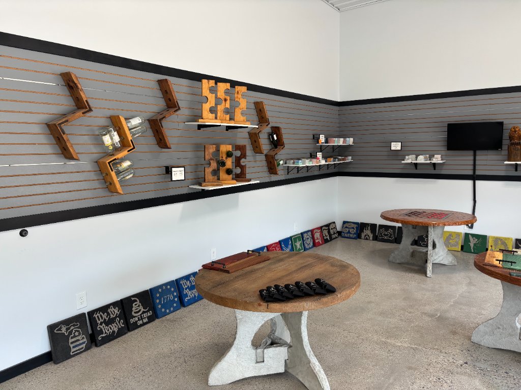 Showroom wall display with wooden wine racks, two round concrete pedestal tables, and decorative patriotic and logo tiles leaning along the base