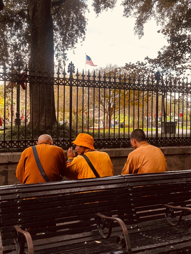Three Buddhist monks in saffron robes seated on a park bench, backs to camera