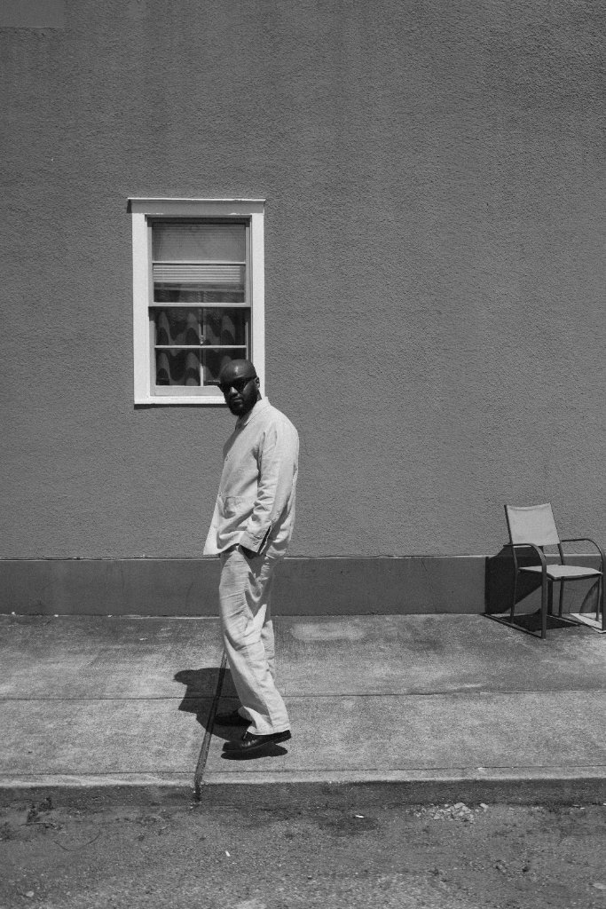 Portrait of a man in light colored clothing against a gray wall with a white window