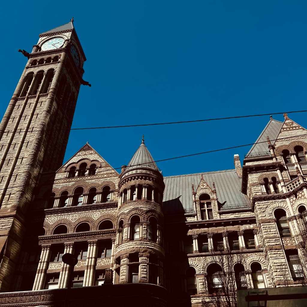 Looking up at an ornate Victorian clock tower and gothic stone building facade against a deep blue sky, power lines crossing the frame