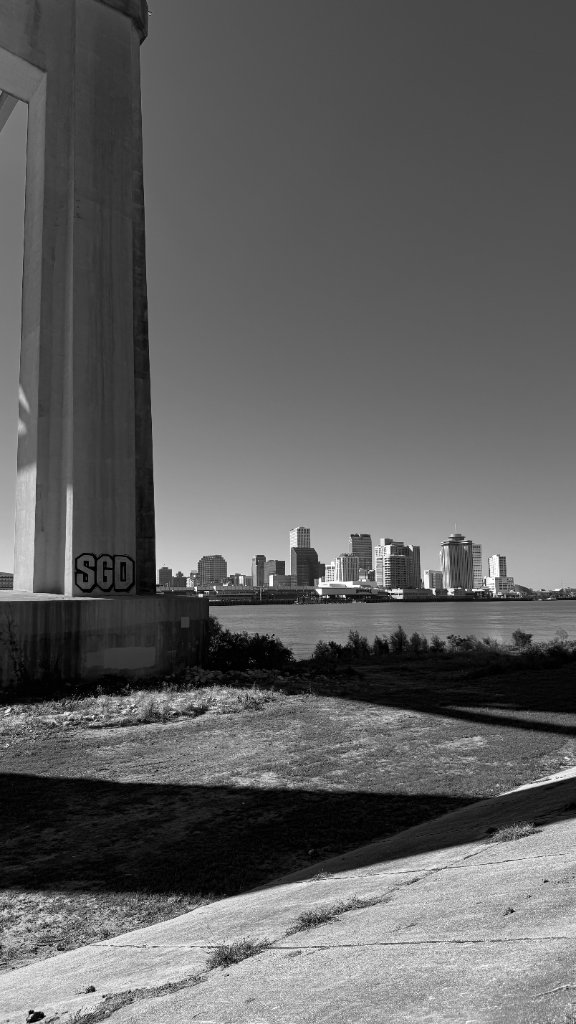 A bridge column tagged SGD frames the New Orleans skyline across the Mississippi River, clear sky, black and white
