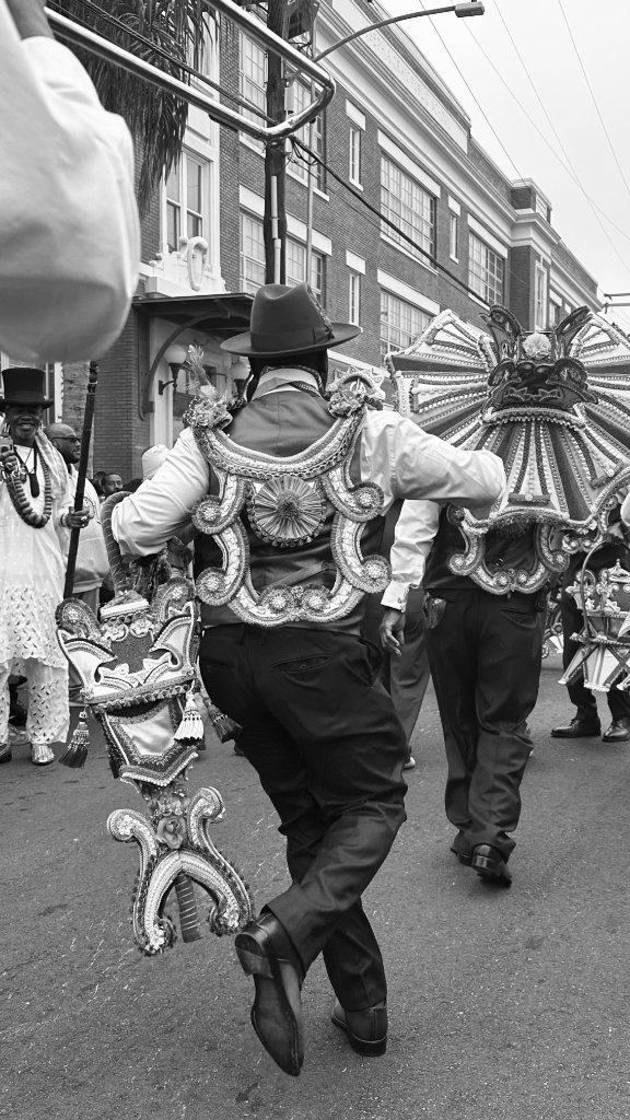 Mardi Gras Indians in elaborate feathered costumes marching through a New Orleans street