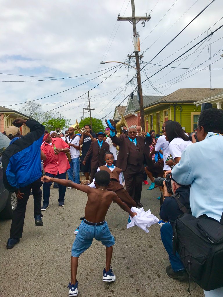 New Orleans second line parade — children dancing in the street as a brass band plays