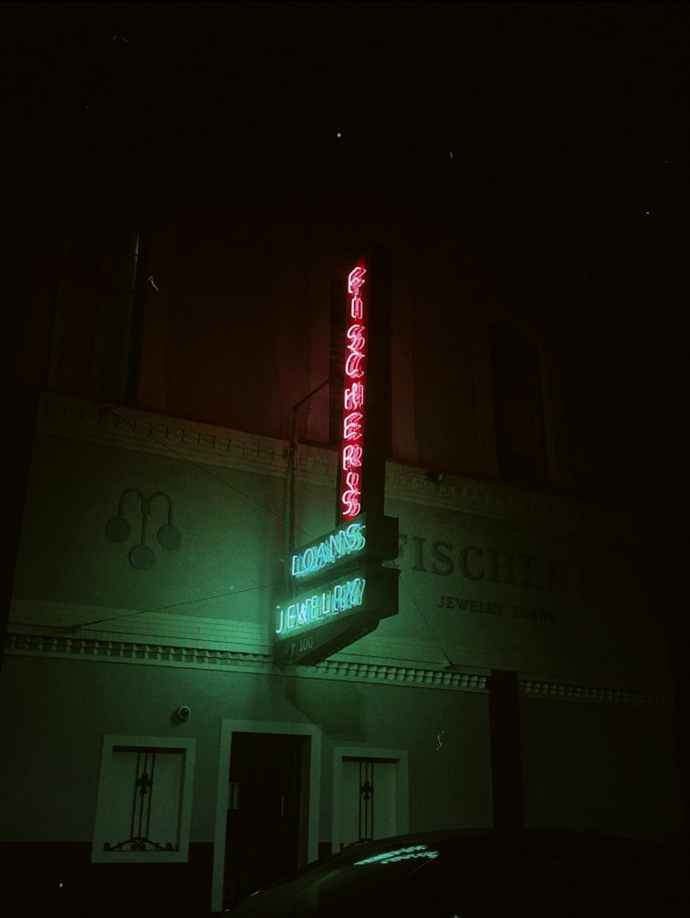 A pink and blue neon sign glowing at night on a vintage building facade, dramatic nighttime urban streetscape