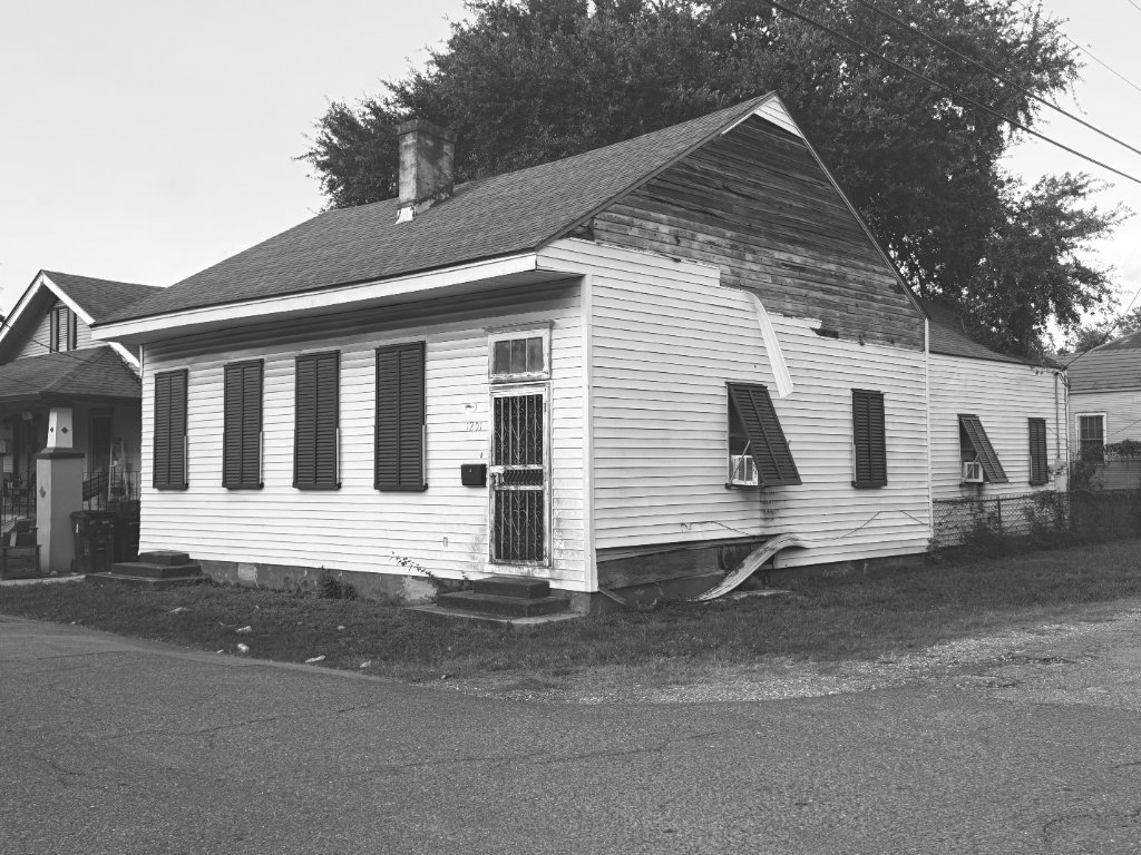 A weathered New Orleans shotgun house, black and white, quiet neighborhood street