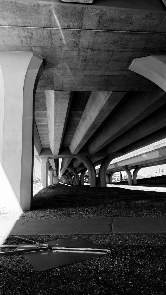 Looking up beneath a concrete highway overpass — columns receding into the distance, dramatic light and shadow