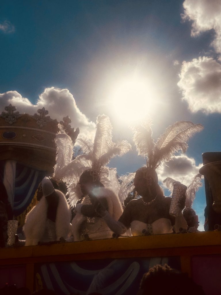 Backlit white feathered angel wings on a Mardi Gras parade float against bright sun and blue sky with clouds
